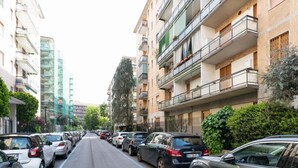 Une rue bordée de voitures garées et d’immeubles résidentiels à plusieurs étages, dotés de balcons et de fenêtres.
