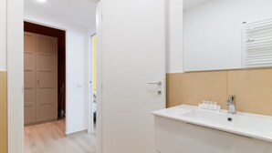 Une salle de bain avec un lavabo blanc, un miroir et une porte donnant sur un couloir.
