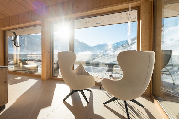 Un interior moderno con ventanas amplias, dos sillas blancas y un techo de madera.