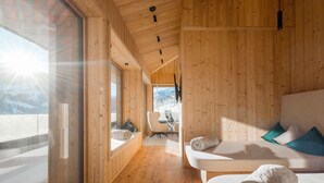 A wooden interior with a sofa, a chair, and a window with a view of a snowy landscape. - Holiday Apartment 'Mountain Suite No°103' with Mountain View, Balcony and Wi-Fi (Großarl)