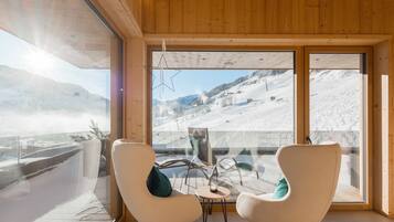 Una stanza con soffitto in legno, ampie finestre vista su una montagna innevata, due sedie e un tavolino.