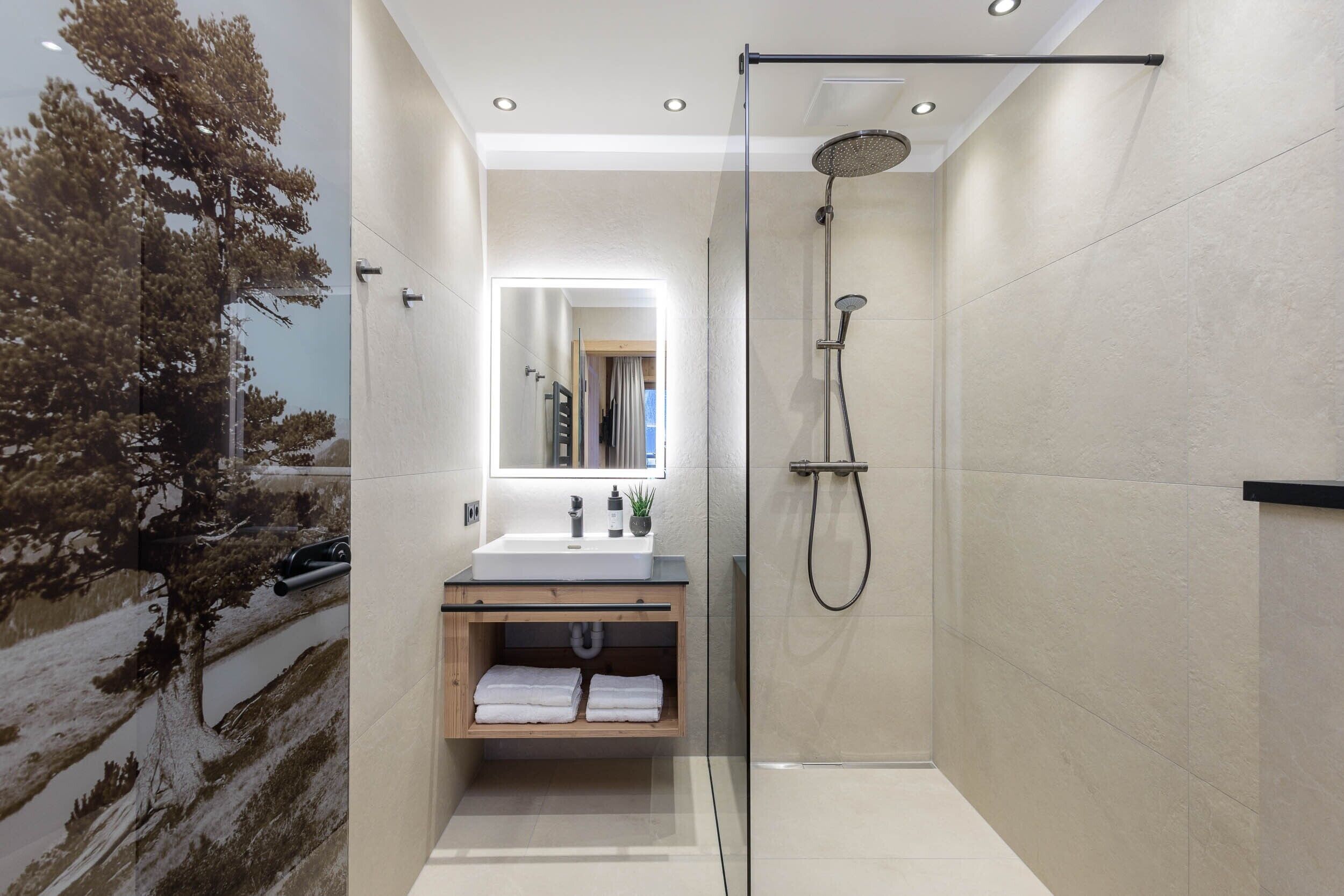 A modern bathroom with a glass-enclosed shower, a sink with a mirror above, and a shelf with towels.