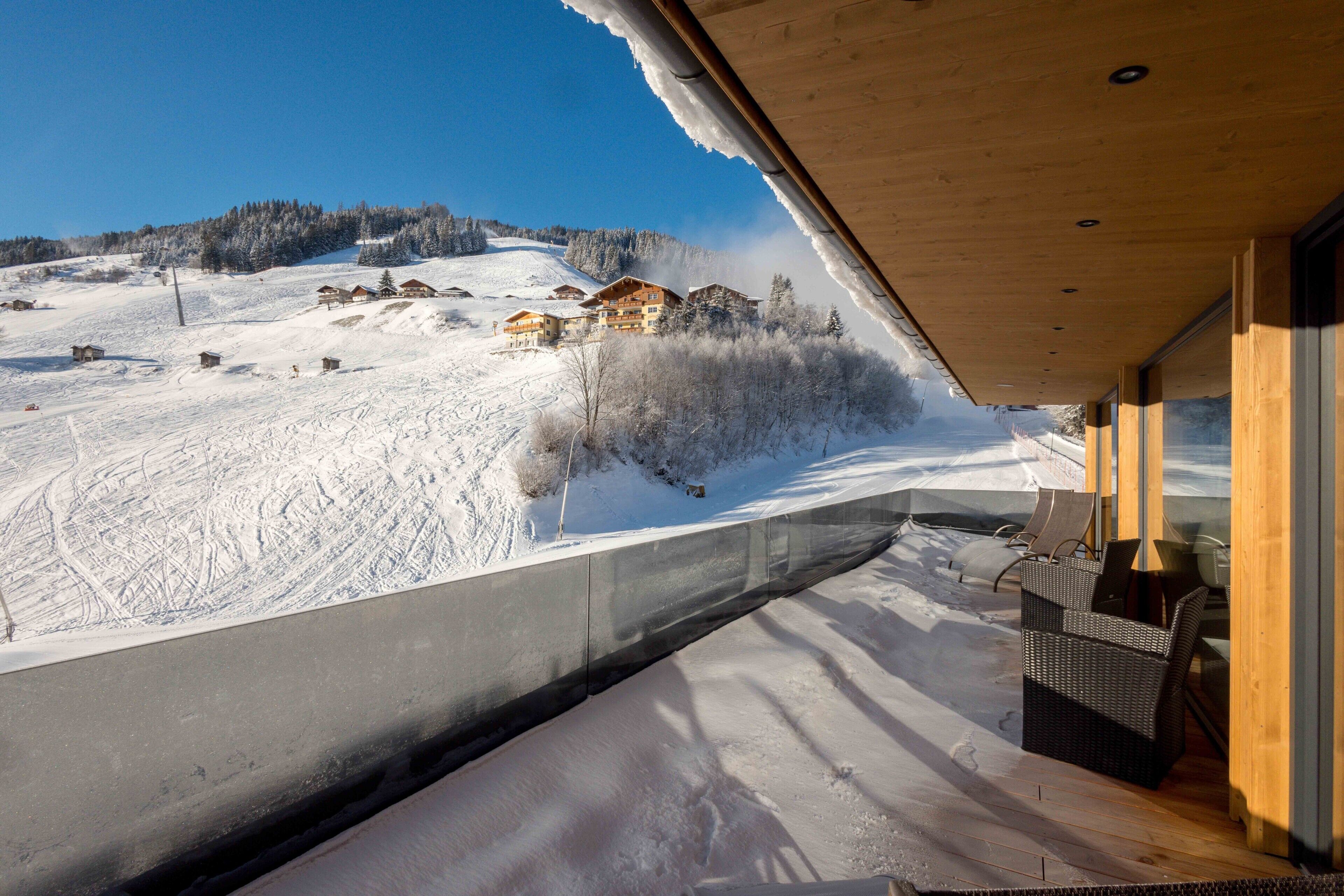 Schneebedeckte Landschaft mit einem Holzbäude und einem Balkon mit Korbmöbeln.