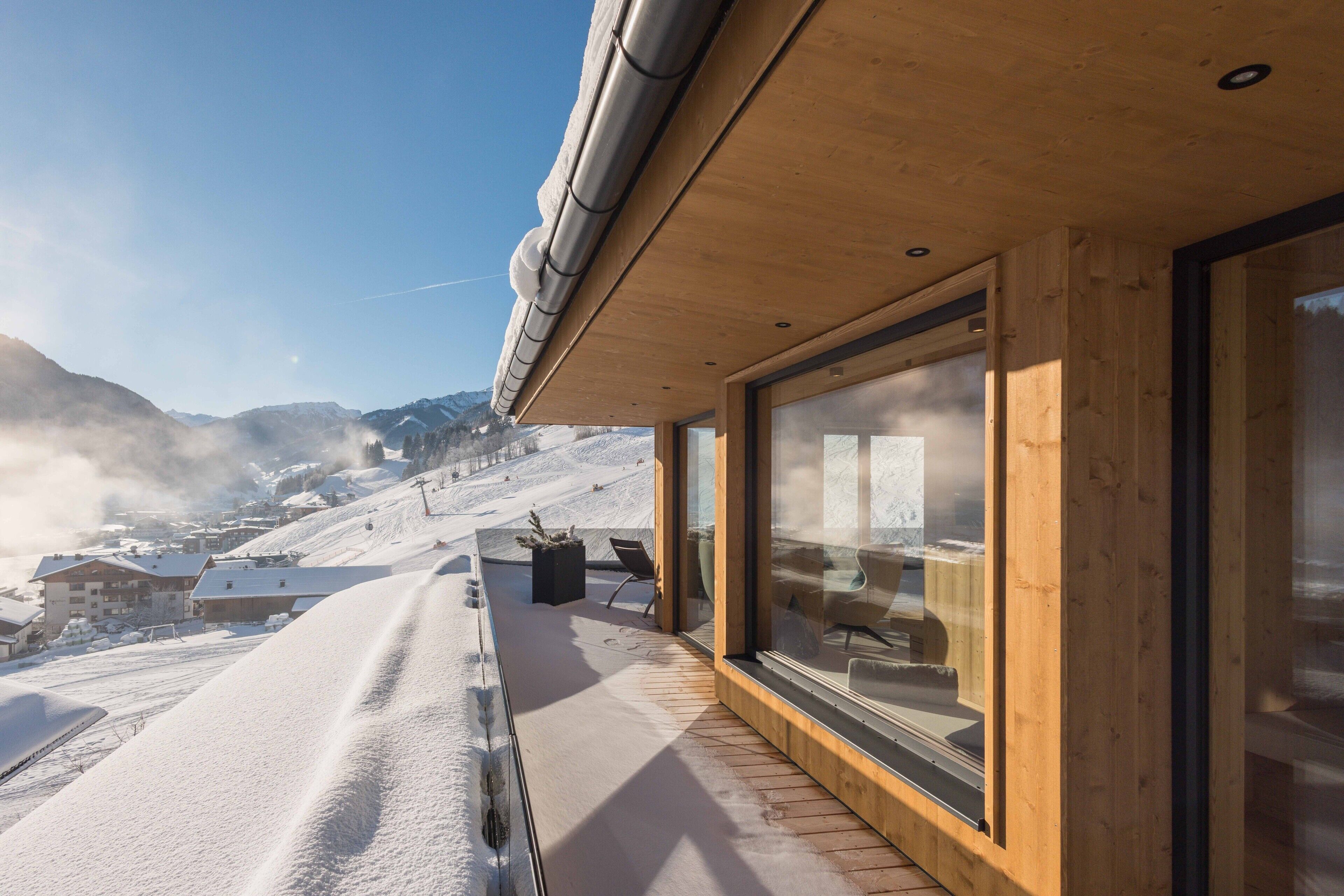 Une façade en bois, de grandes fenêtres en verre, une pente enneigée et un ciel dégagé.