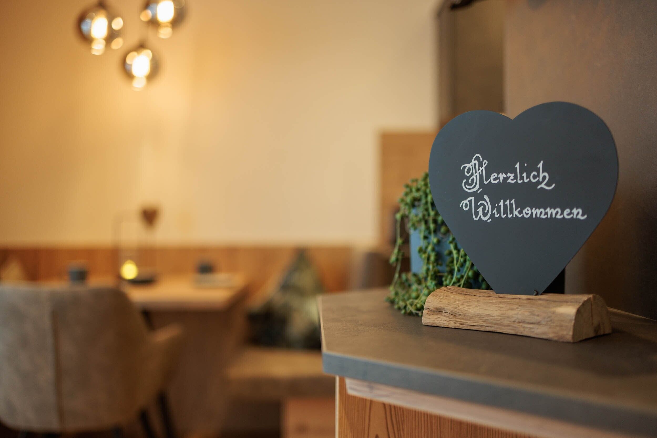 A heart-shaped sign with 'Herzlich Willkommen' on a wooden stand in a restaurant setting.