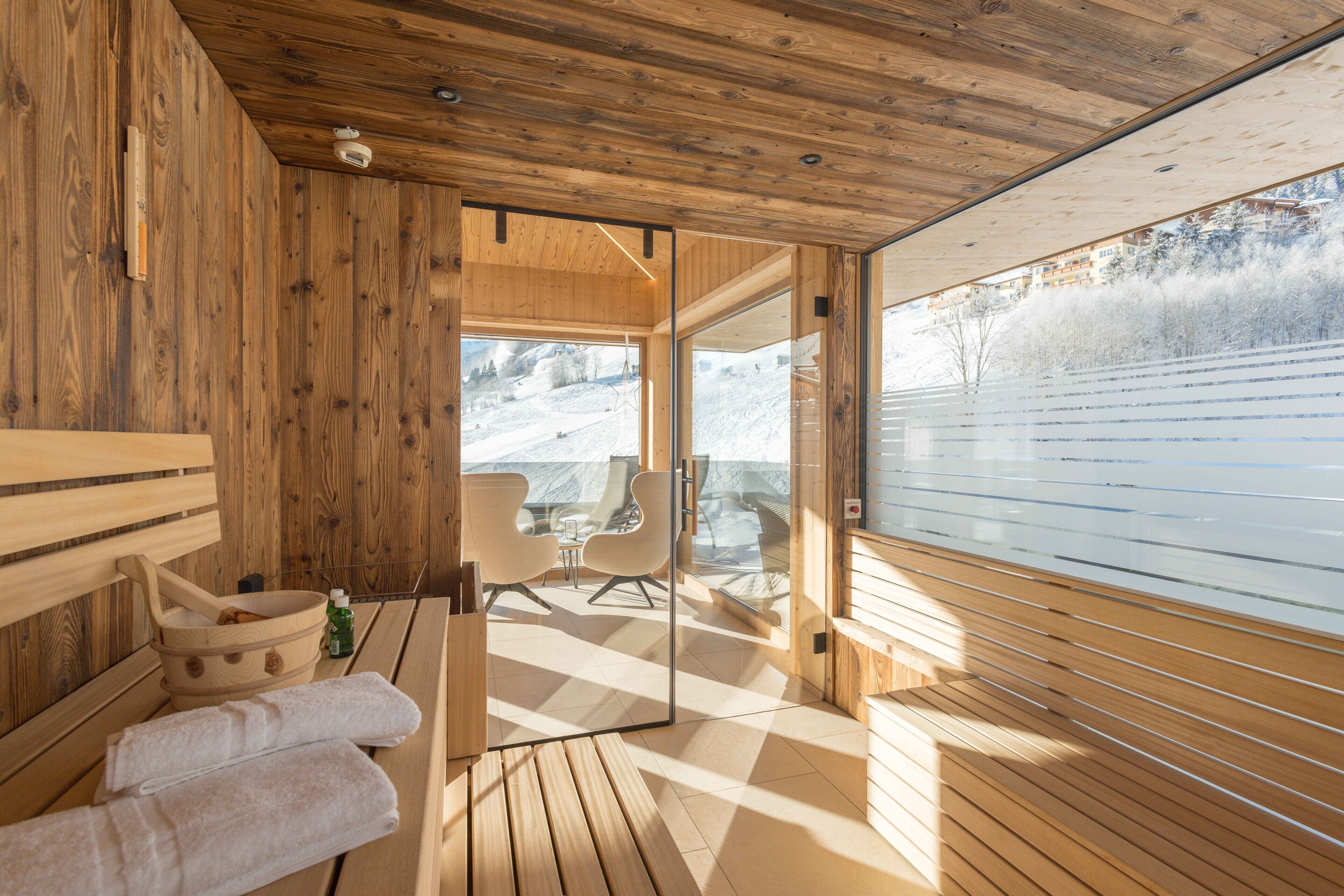 A wooden interior with a sauna, a wooden bench, and a glass door leading to a balcony with a view of a snowy landscape.