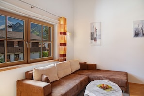 A modern living room with a brown sofa, a small round table, and a window with a view of mountains.