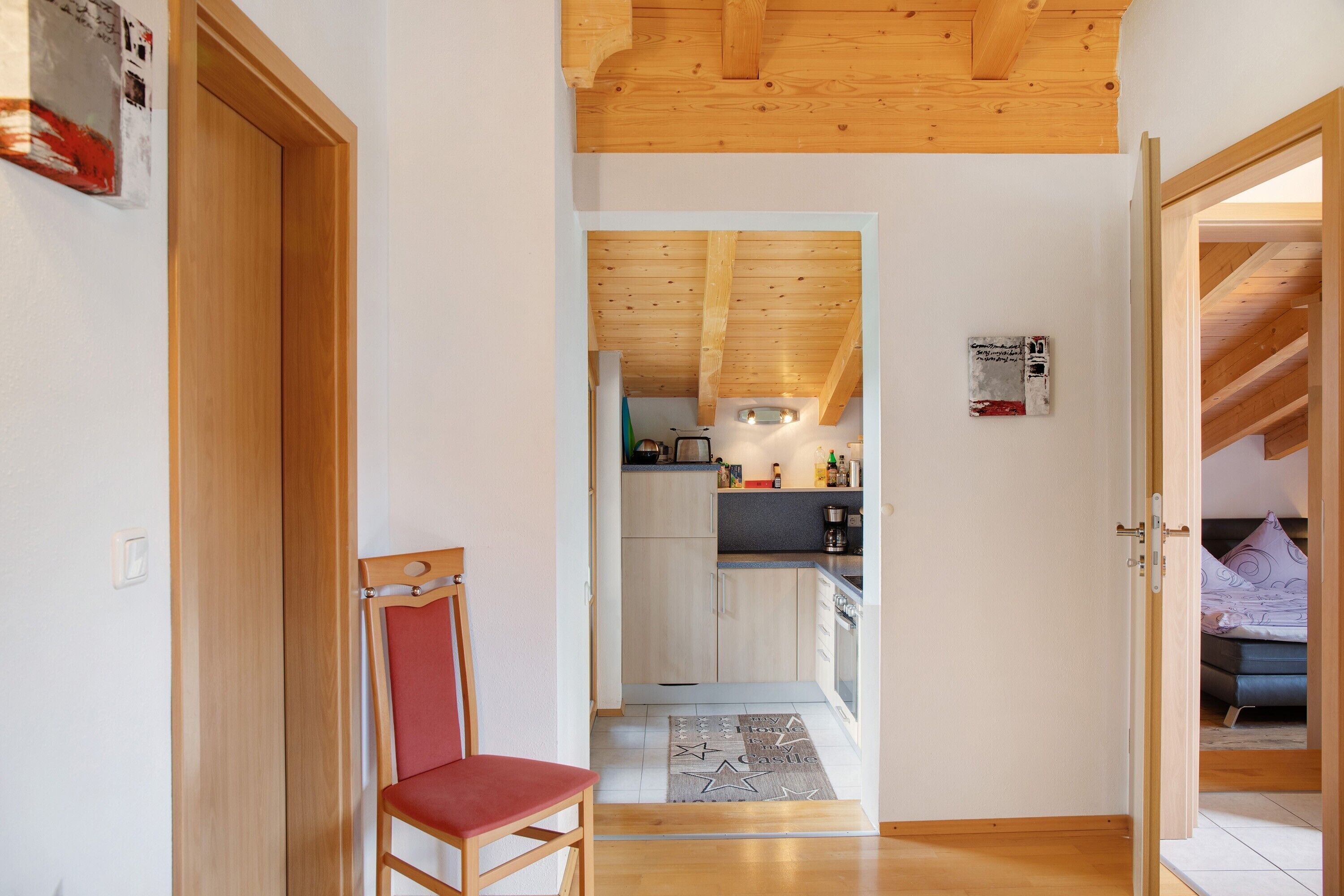 A wooden interior with a kitchen, a dining area with a chair, and a bedroom with a bed.