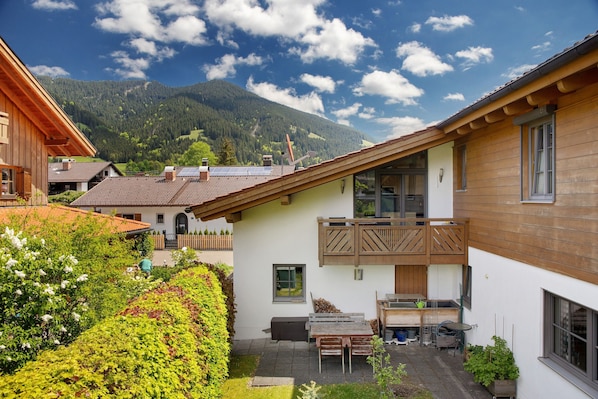 A residential building with a balcony, a patio area with a table and chairs, and a view of a mountainous landscape.