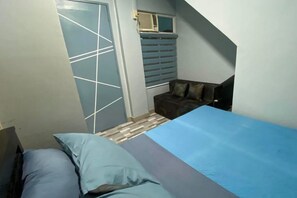 A bedroom with a bed, a window with blinds, a door, and a small seating area with cushions. - 2BR at Amplayo Apartelle — Modern comfort, cozy vibes at an affordable price... (Cagayan de Oro City)