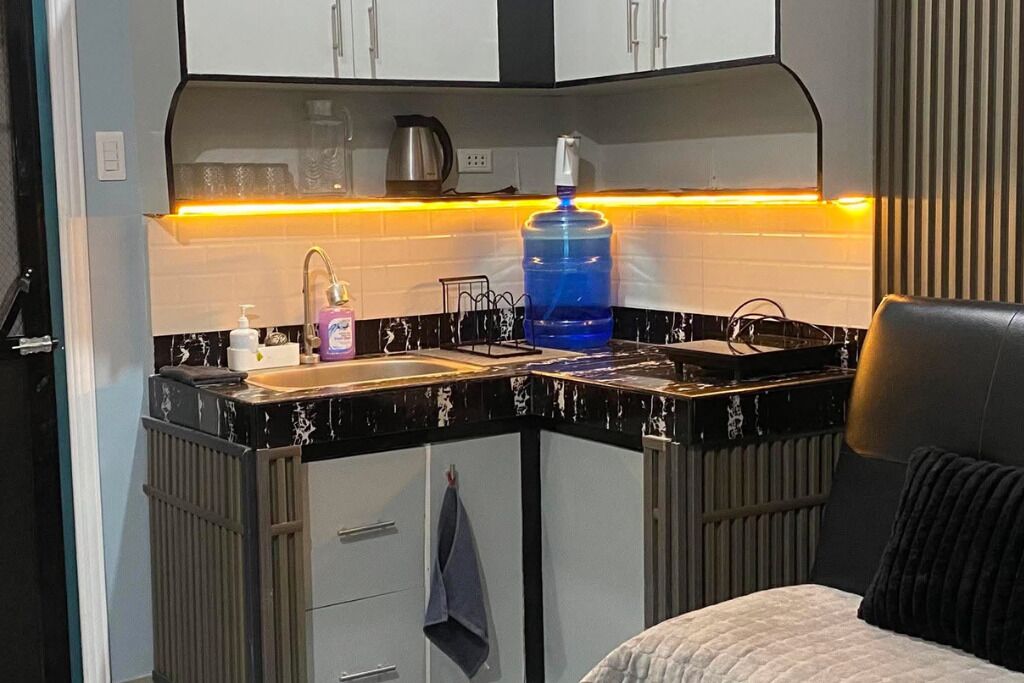 Uma cozinha compacta com pia, chaleira, um grande reservatório de água e bancada com diversos itens.
