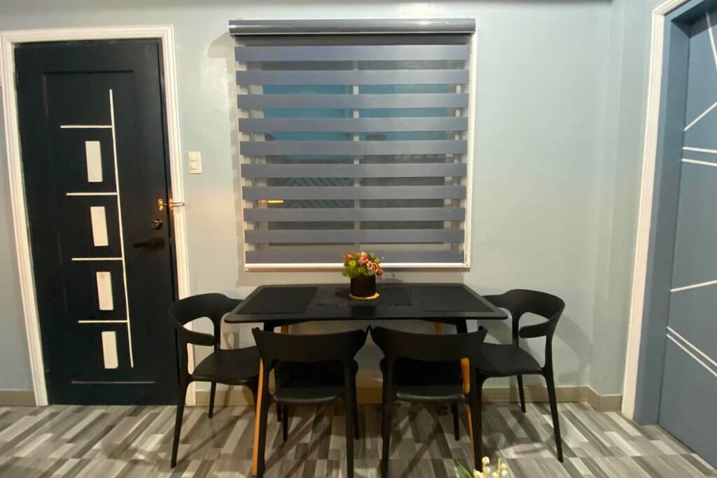 Uma sala de jantar com mesa e cadeiras pretas, uma janela com persianas e uma porta com design geométrico.