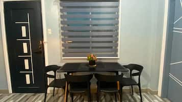 Uma sala de jantar com mesa e cadeiras pretas, uma janela com persianas e uma porta com design geométrico.