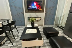 A room with a TV mounted on the wall, a small table with a plant, black chairs, and a sofa. - 2BR at Amplayo Apartelle — Modern comfort, cozy vibes at an affordable price... (Cagayan de Oro City)
