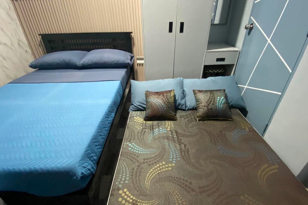 A single bed with a blue bedspread and two pillows, a wardrobe with two doors, and a small bedside table with a drawer.