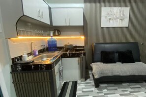 A compact room with a kitchenette, a bed, and a cityscape artwork on the wall. - 2BR at Amplayo Apartelle — Modern comfort, cozy vibes at an affordable price... (Cagayan de Oro City)