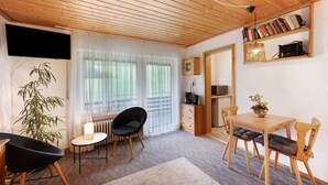 Um quarto com teto de madeira, uma mesa de jantar com cadeiras, uma cadeira preta, um radiador, uma planta e uma estante de livros.