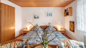 Quarto com teto de madeira, cama com roupa de cama xadrez, duas mesas de cabeceira com luminárias e arte na parede.