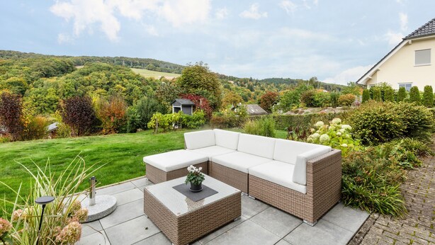 A garden with a wicker sofa and a round table, surrounded by greenery and a view of hills. - Apartment 'Fischer' with Mountain View, Private Terrace and Wi-Fi (Diemelsee)