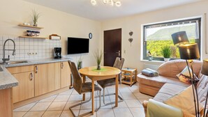 A compact living space with a kitchen, dining area, and a sofa by a window. - Apartment 'Fischer' with Mountain View, Private Terrace and Wi-Fi (Diemelsee)