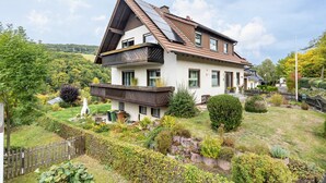 A two-story house with a sloped roof, solar panels, and a garden with various plants and a statue. - Apartment 'Fischer' with Mountain View, Private Terrace and Wi-Fi (Diemelsee)