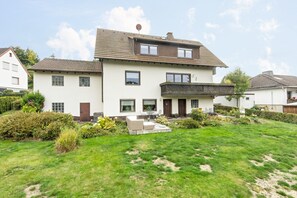 A two-story house with a well-maintained lawn, a patio with outdoor furniture, and a satellite dish on the roof.