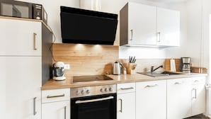 Una cocina moderna con armarios blancos, encimera de madera, horno empotrado, cafetera y microondas.