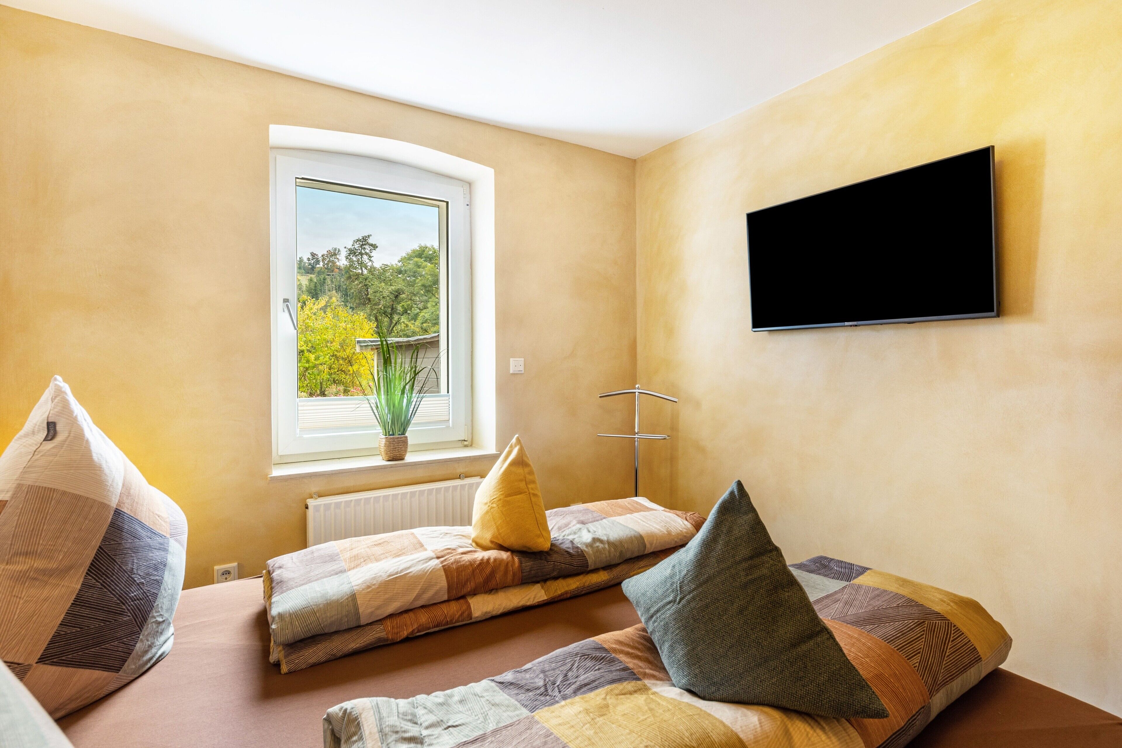 Ein Zimmer mit einem Bett, einem Fenster und einem an der Wand befestigten Fernseher.