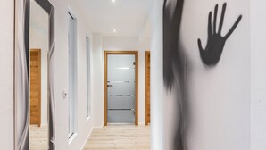 Un pasillo con piso de madera, una puerta de cristal y una huella en la pared.