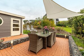 Eine Terrassengruppe mit Korbmöbeln, einem Glastisch und einem weißen Baldachin.