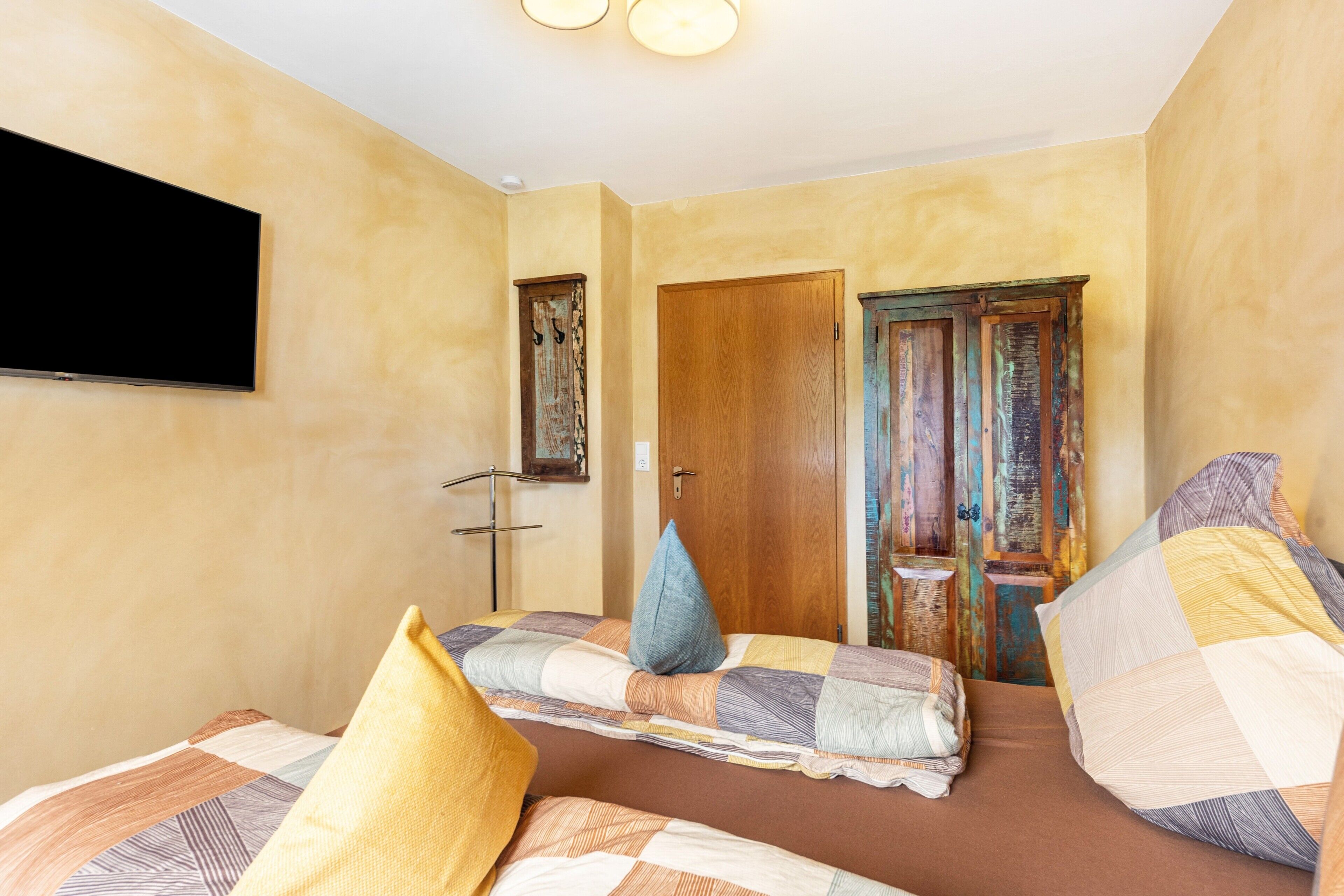 A bedroom with two beds, a television, a wooden door, and a small table.