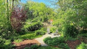 Un jardin avec un chemin dallé, différentes plantes et une clôture en bois.