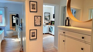 Un couloir menant à une cuisine, avec des tableaux encadrés accrochés au mur, un plancher en bois et un grand miroir.