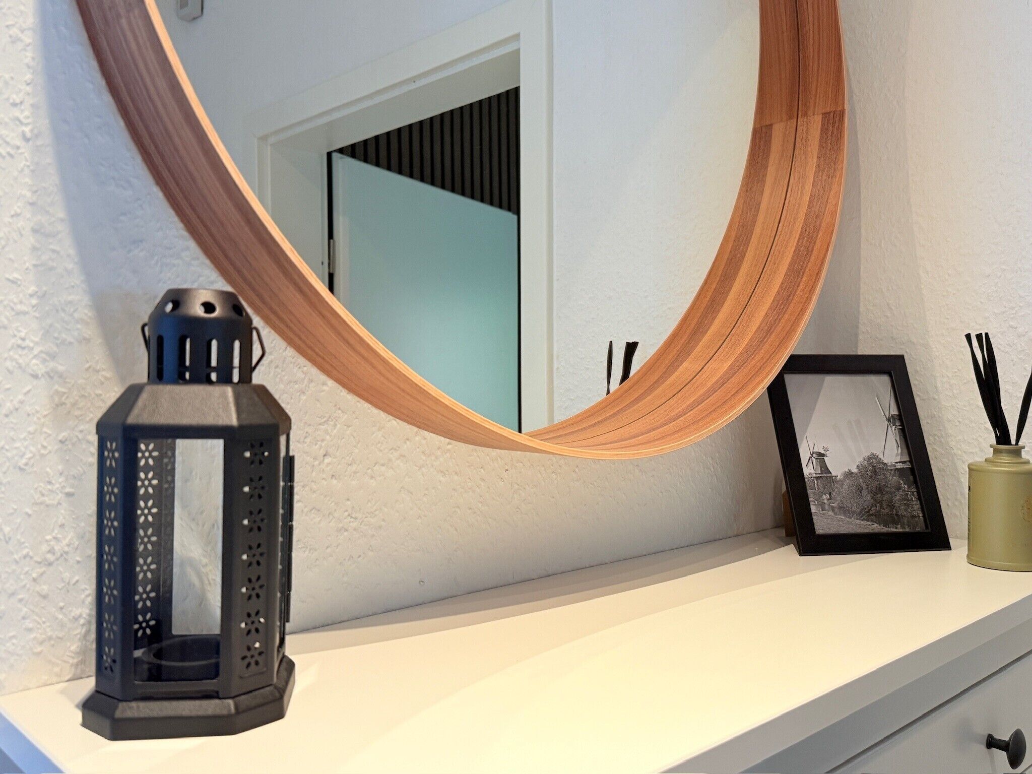 Ein Spiegel mit Holzrahmen, ein schwarzer Laternen, ein gerahmtes Foto und eine Vase mit schwarzen Ästen.