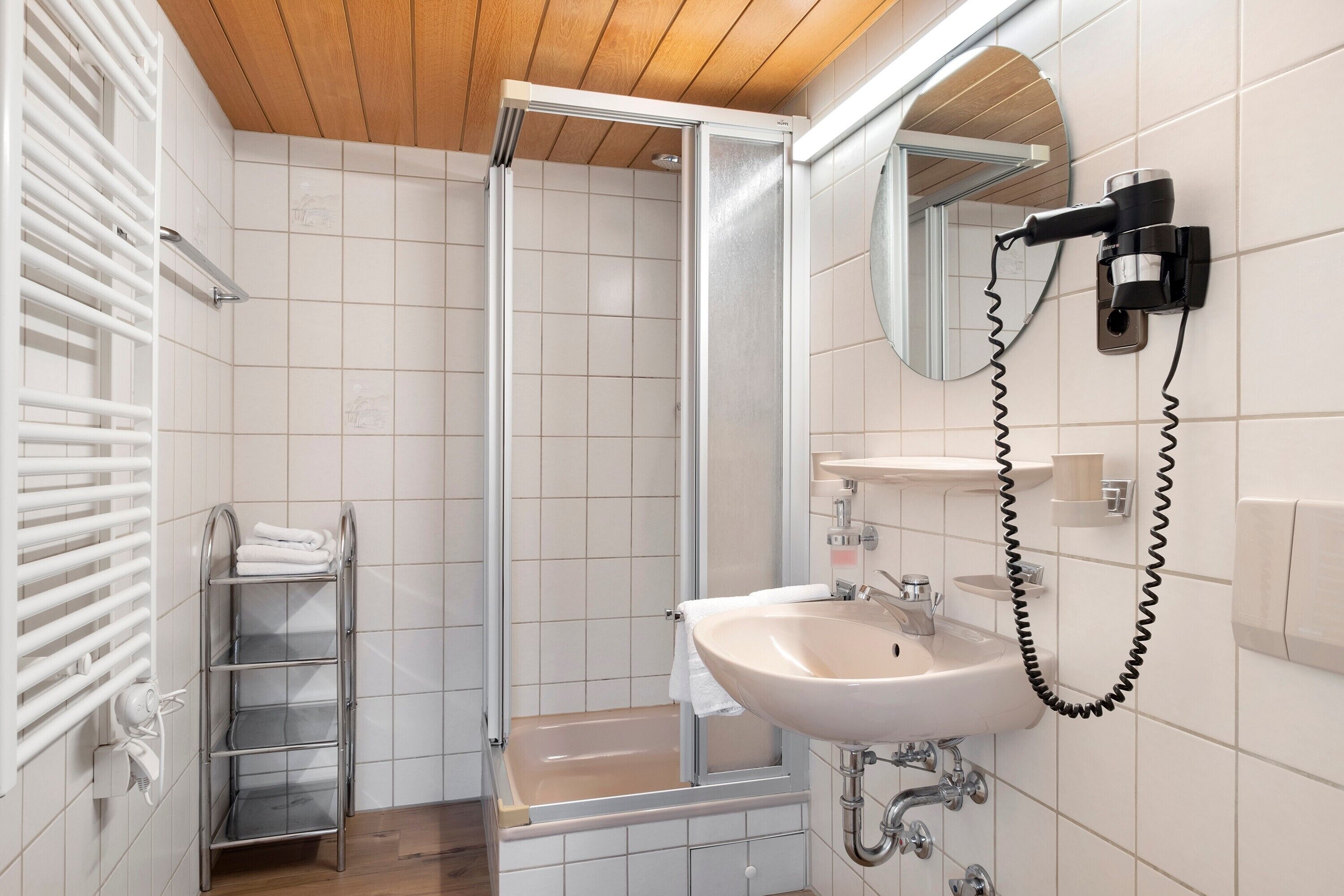 A bathroom with a shower, a sink, a towel rack, and a mirror.