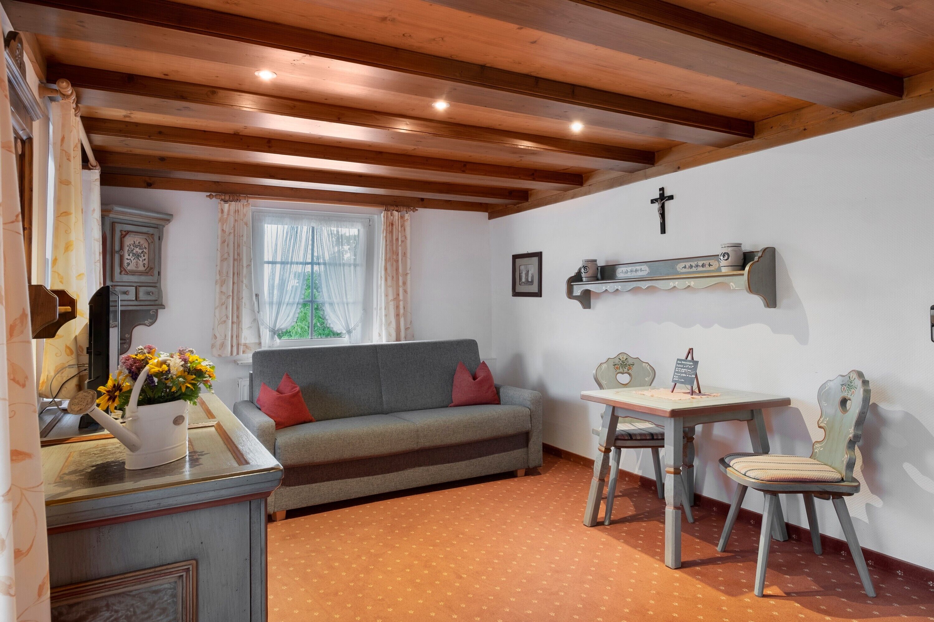 Una habitación acogedora con techo de madera, un sofá, una mesa con una silla y una ventana con cortinas.
