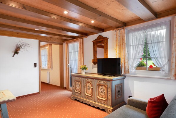A wooden-paneled room with a television on a cabinet, a sofa, and a window with curtains.