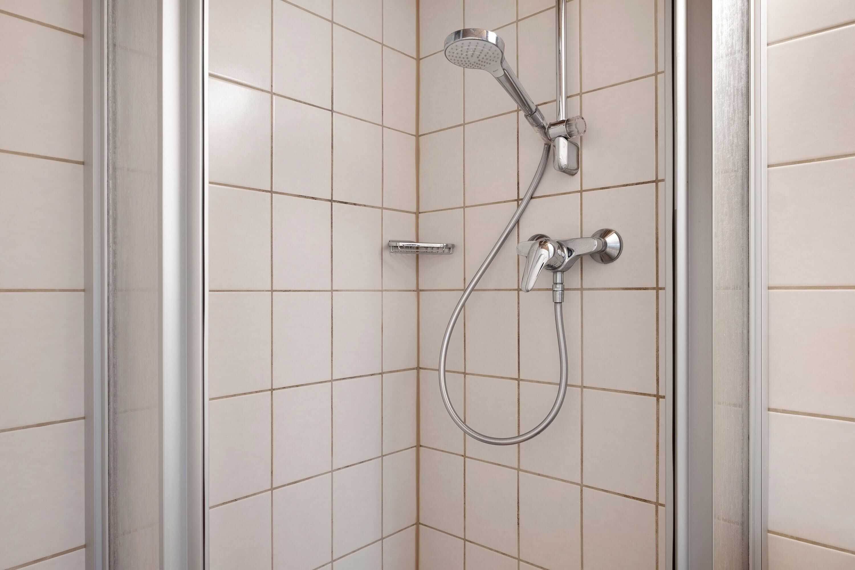 Une douche équipée d’un pommeau de douche à main et d’un robinet mural dans une salle de bain carrelée.