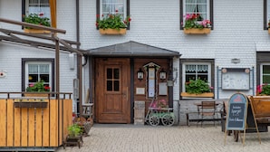 A building with a wooden door, windows with flower boxes, a signboard, and a cart. - Room 'Nr 7' with Mountain View, Shared Terrace and Wi-Fi (Titisee-Neustadt)