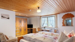 Quarto com teto de madeira, cama com roupa de cama floral, escrivaninha, televisão e guarda-roupa.