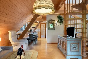 Un intérieur en bois comprenant un escalier, un coin repas et un téléviseur posé sur un meuble.