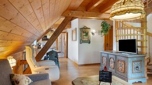 A wooden ceiling, a sofa, a television on a cabinet, and a staircase.