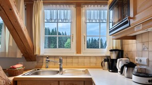 A kitchen with a sink, wooden cabinets, a window with curtains, and various appliances.