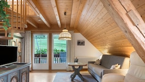A cozy room with a wooden ceiling, a sofa, a television on a cabinet, and a table with a sign.