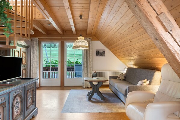 Une pièce chaleureuse avec un plafond en bois, un canapé, un téléviseur posé sur un meuble et une table sur laquelle est placé un panneau.