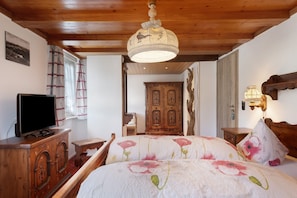A bedroom with a wooden ceiling, a television on a cabinet, a bed with floral bedding, and a wooden wardrobe.
