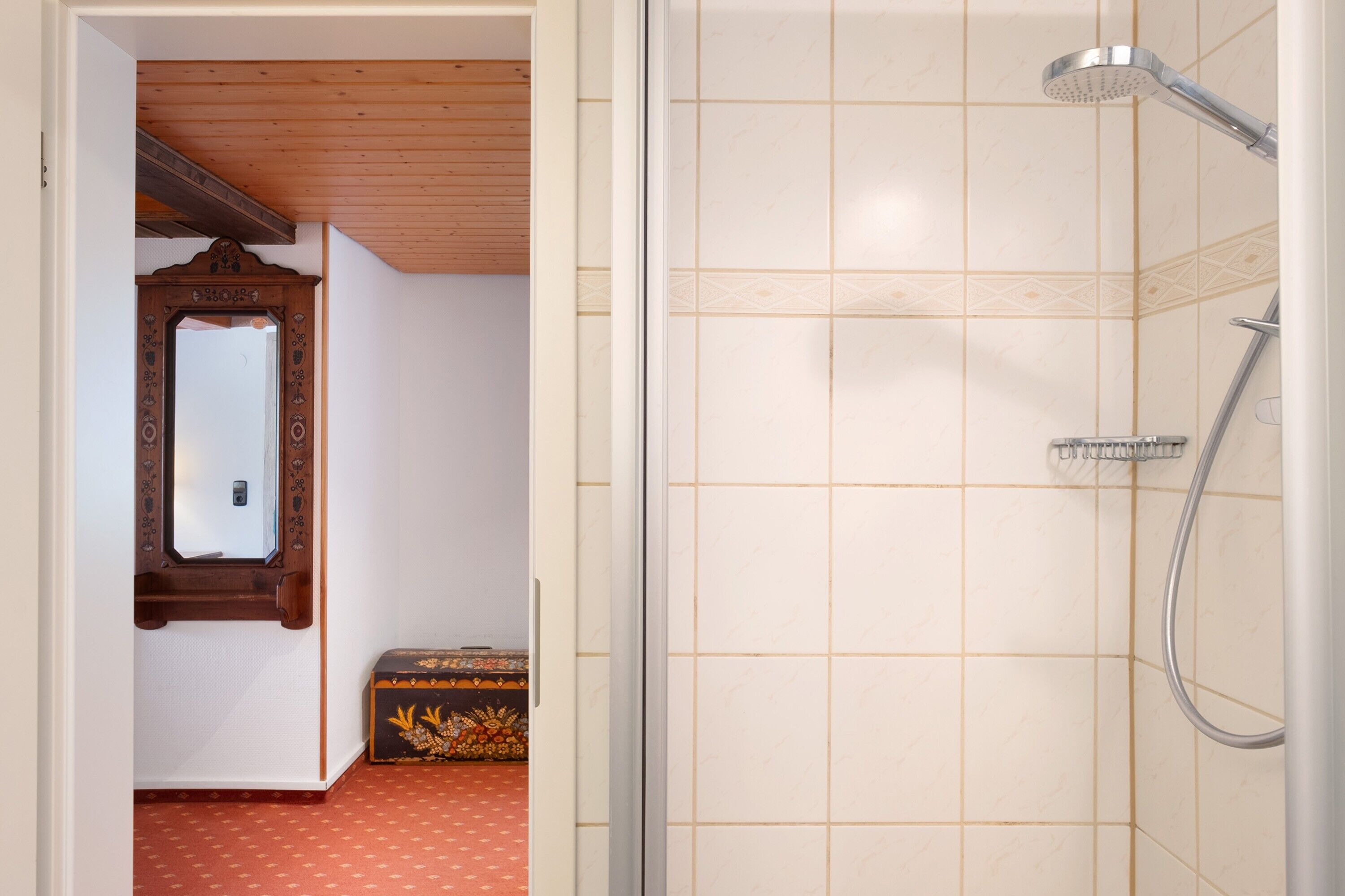 Una ducha con cabezal de ducha de mano, techo de madera y pared con azulejos.