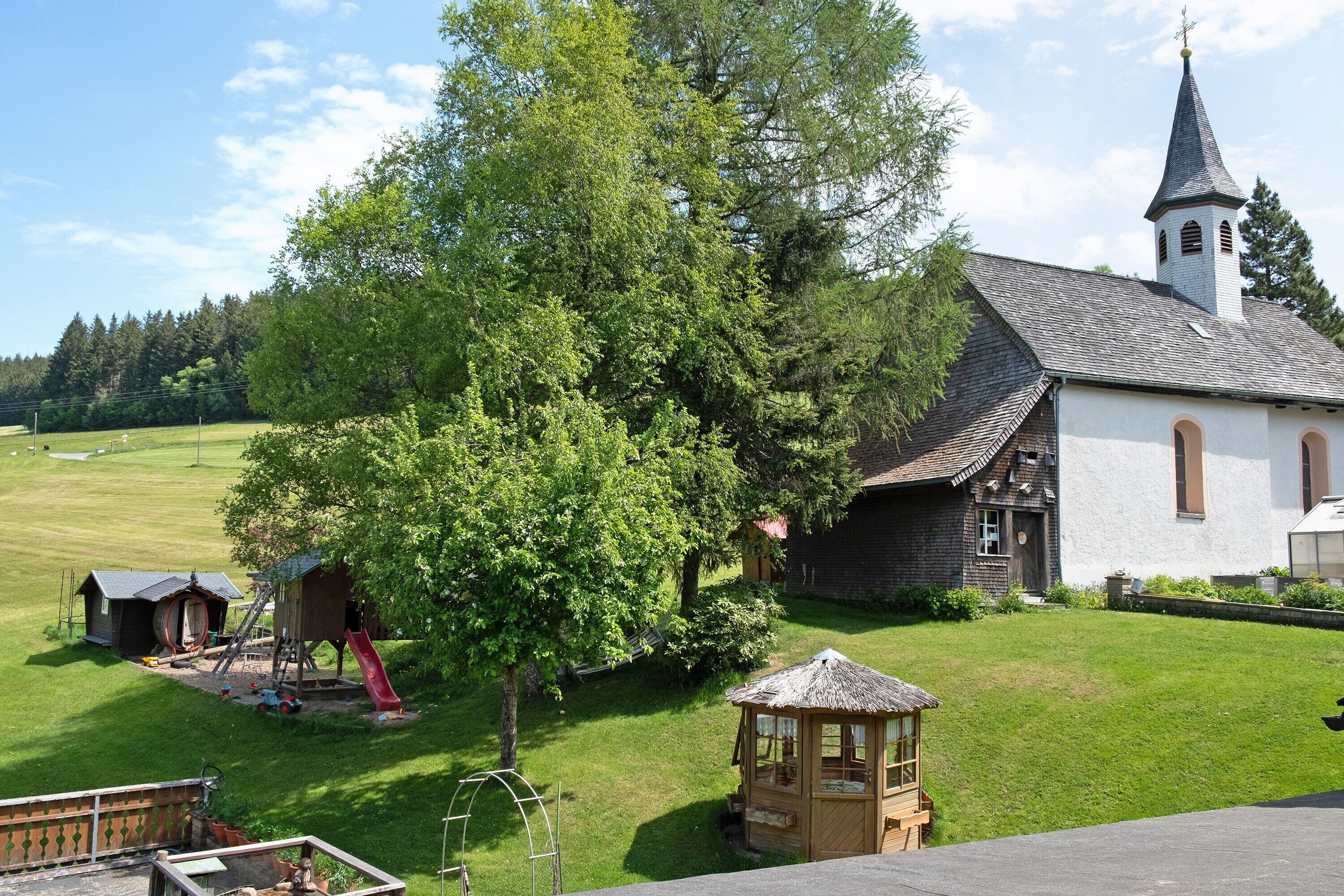A church with a steeple, a playground, and a gazebo in a grassy area.