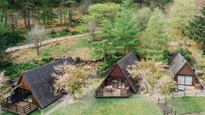 Three cabins with sloped roofs, surrounded by dense forest. Each cabin has a deck with outdoor seating. - Heron Lodge by Interhome (Invergarry)