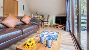 A cozy living room with a brown leather sofa, a coffee table with a Monopoly board game, and a TV in the background. - Heron Lodge by Interhome (Invergarry)
